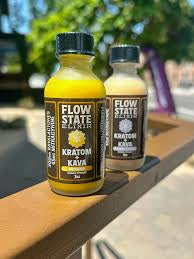 Two bottles of Flow State Kratom Kava on a wooden surface with a blurred outdoor background.